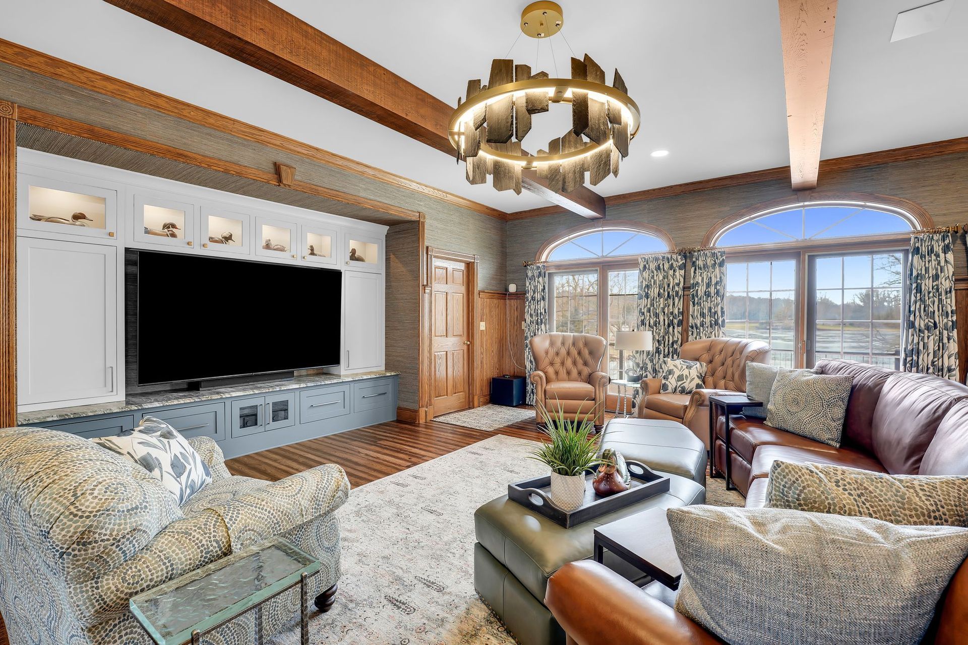 Living room with large TV, leather couches, and arched windows.