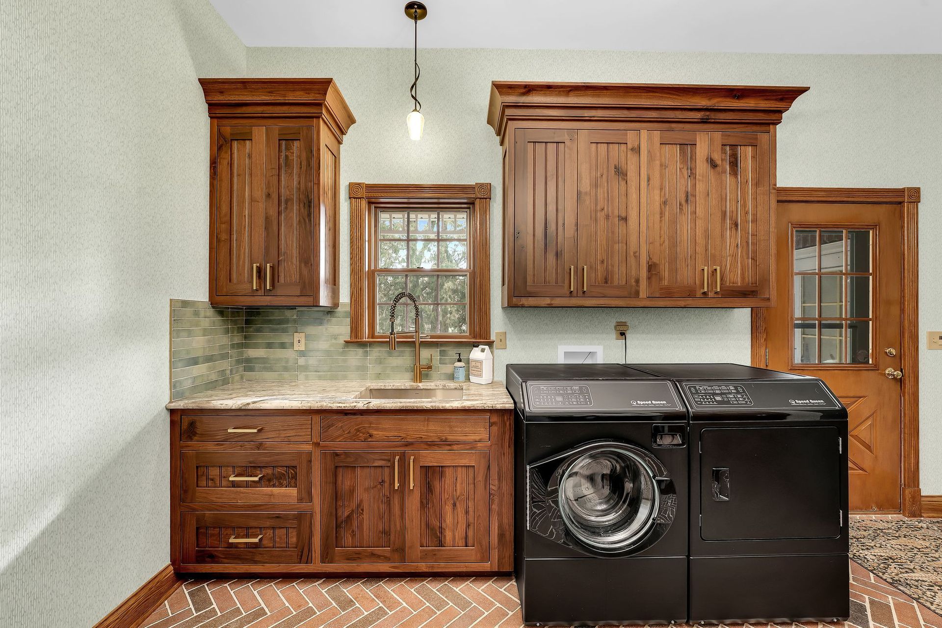 Laundry room with brown cabinets, sink, washer/dryer, and a door, all under a light.