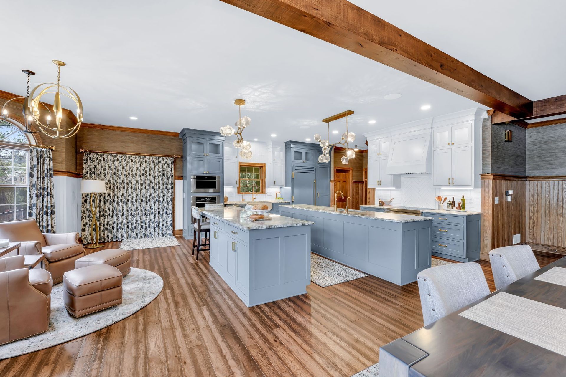 Open-concept kitchen with blue cabinets, multiple islands, hardwood floors, and exposed wooden beams.