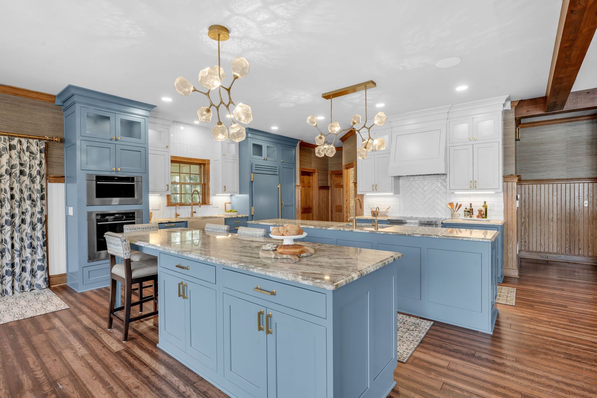 Blue and white kitchen with two islands, gold light fixtures, and wood floors.