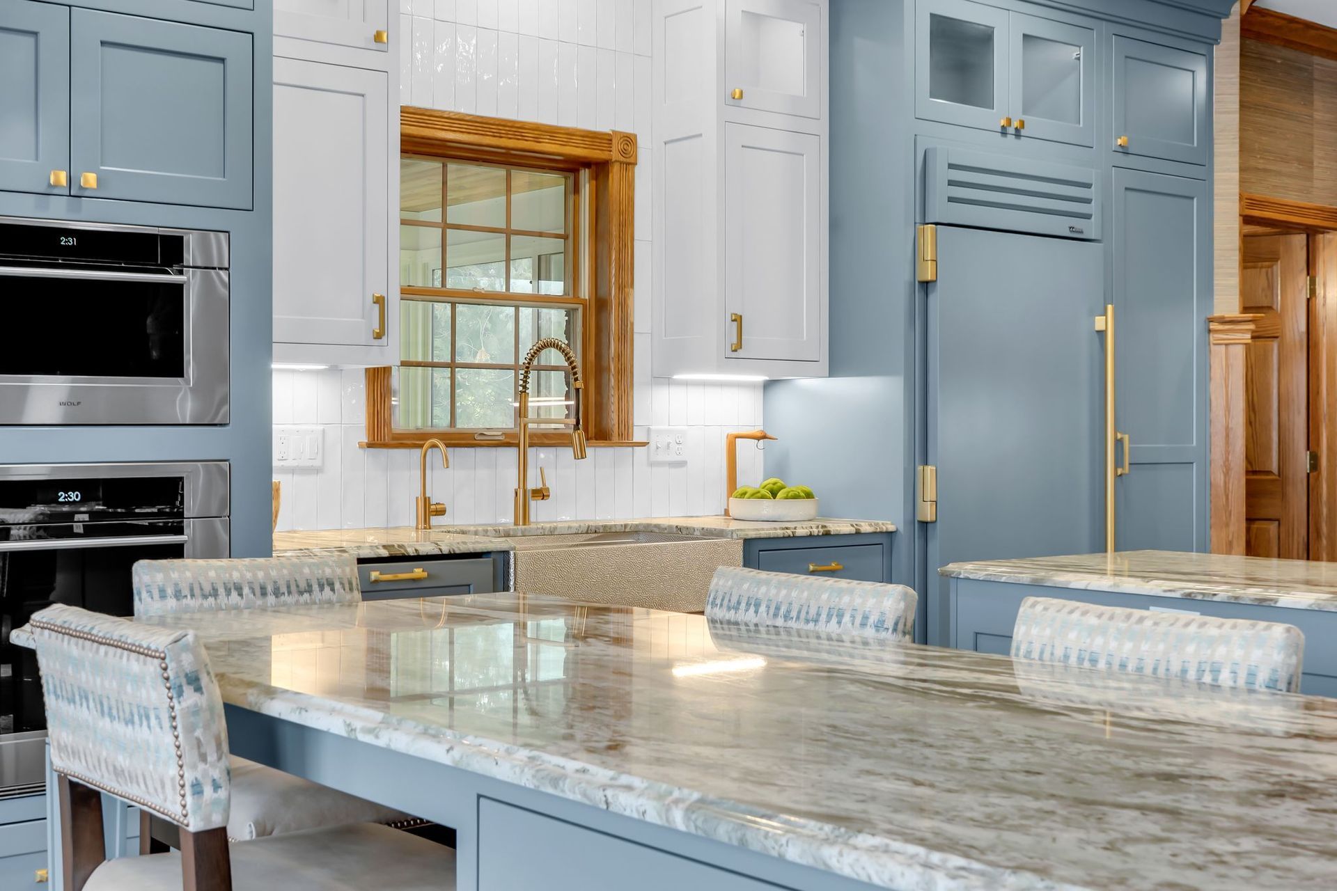 Elegant kitchen with blue and white cabinets, gold hardware, and a granite countertop island.