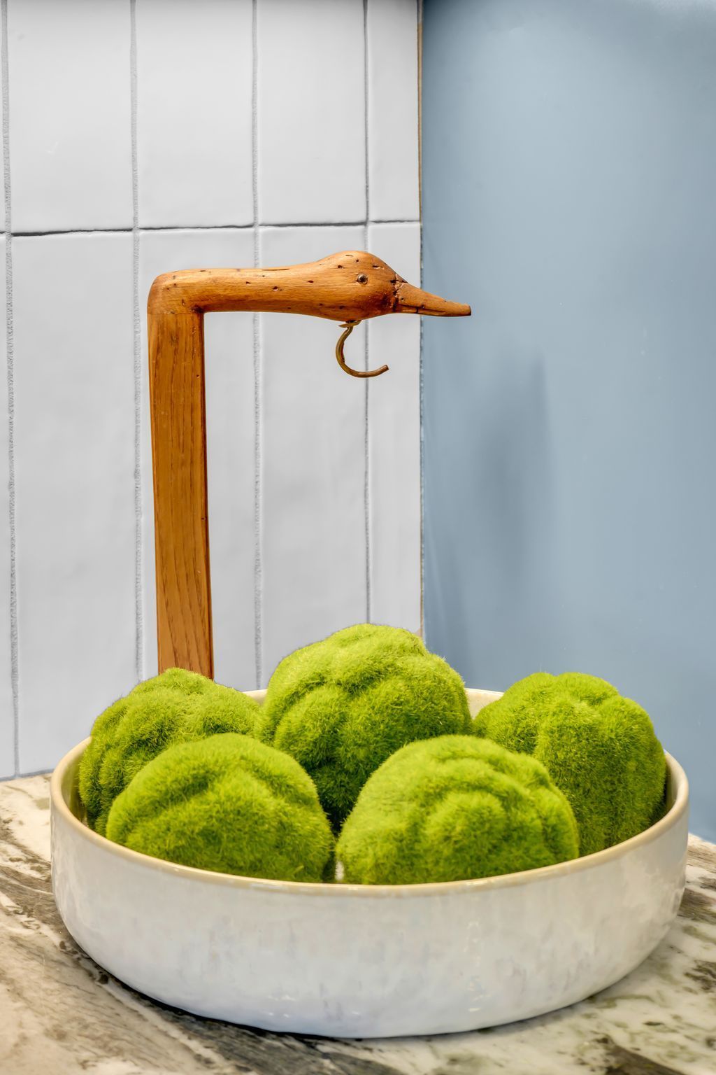 White bowl with mossy green spheres, next to a wooden bird-shaped hook stand.