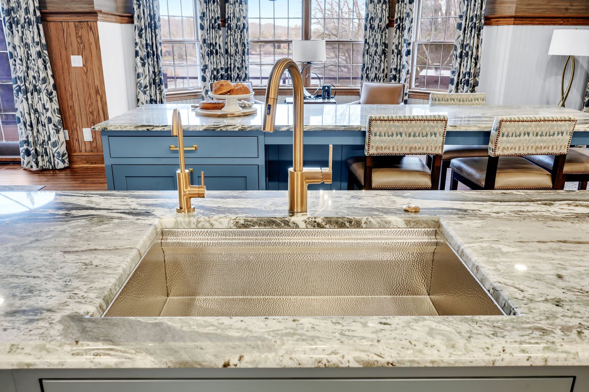A kitchen with a large sink, gold faucet, and blue island with chairs.
