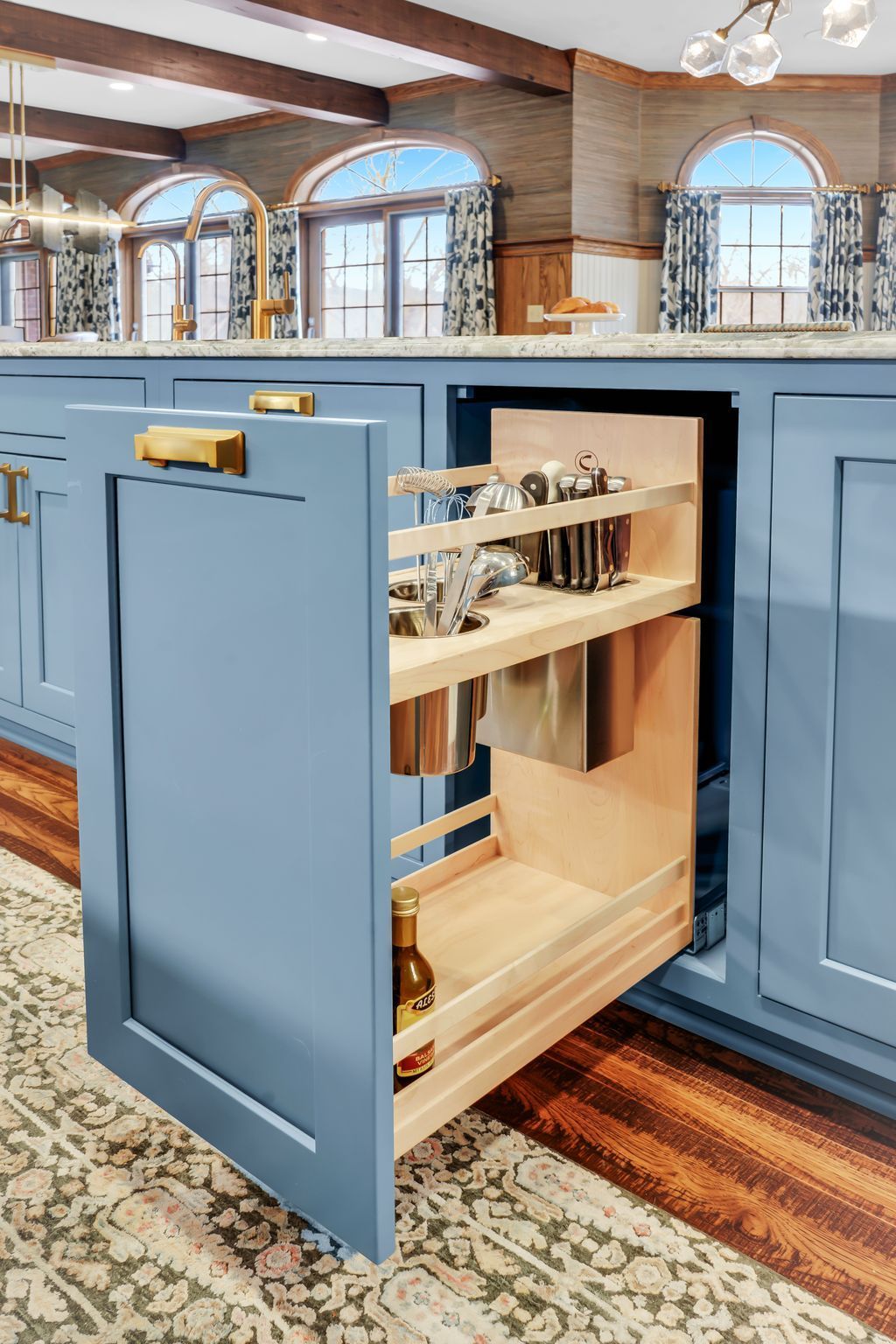 Blue kitchen cabinet with pull-out spice rack. Interior with items displayed, a modern gold handle, and beige carpet.