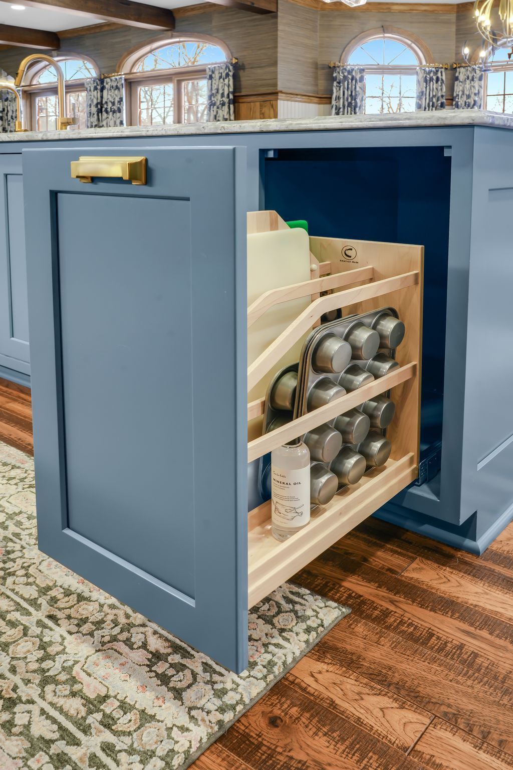 Blue kitchen cabinet with a pull-out organizer holding muffin tins and other baking supplies.
