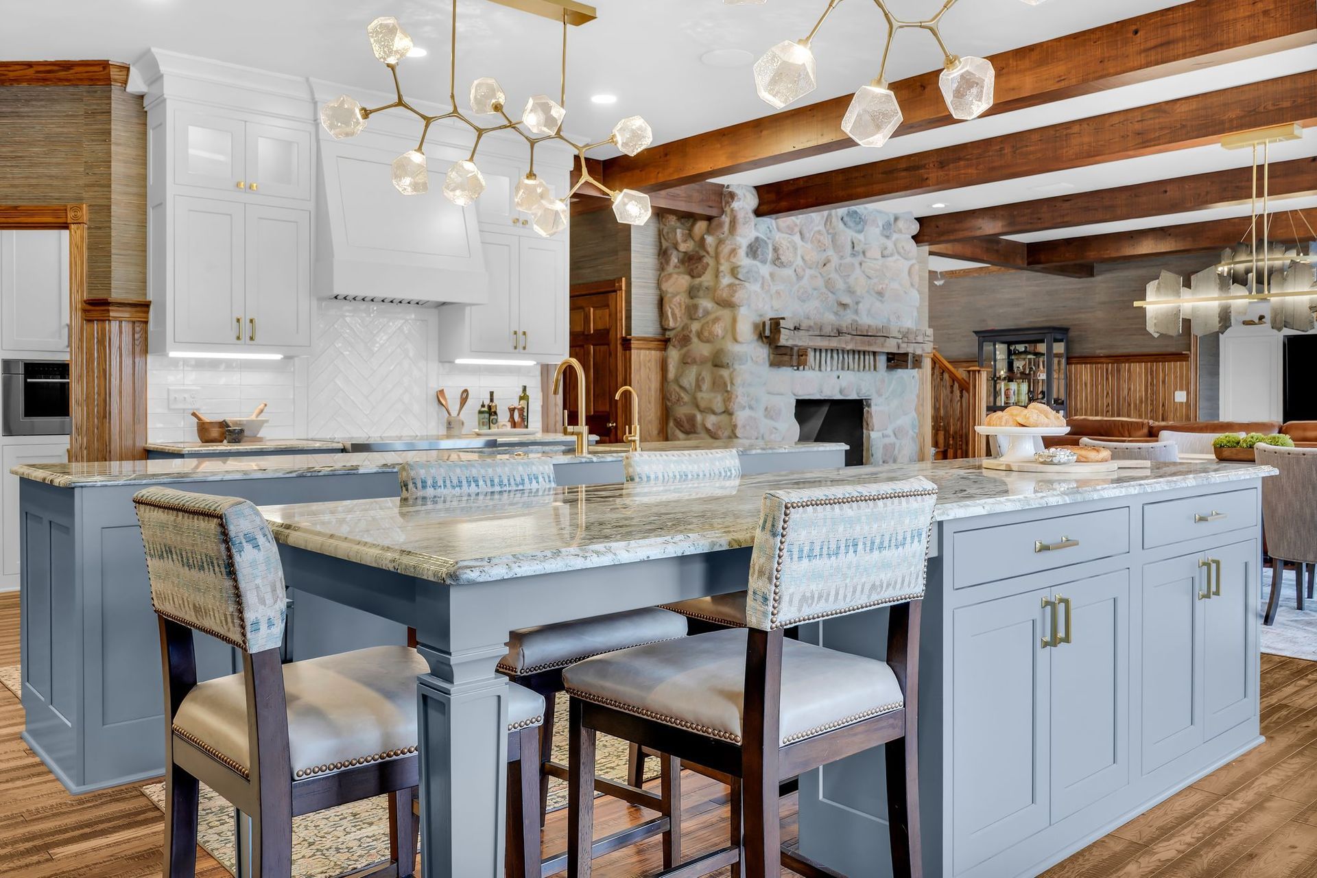 Kitchen with blue island, white cabinets, stone fireplace, and gold light fixture.