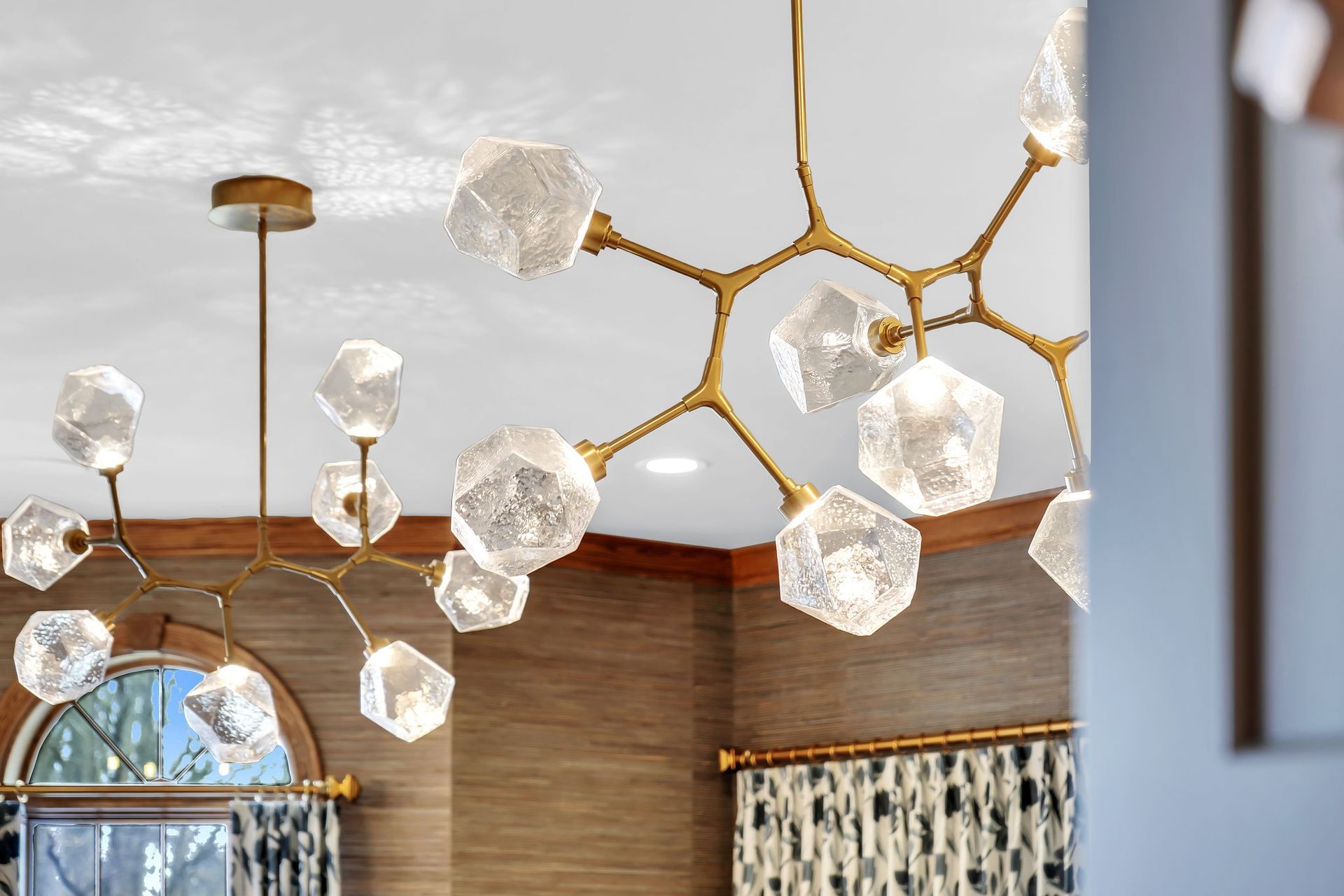 Two modern gold chandeliers with geometric crystal lights hang from a ceiling.