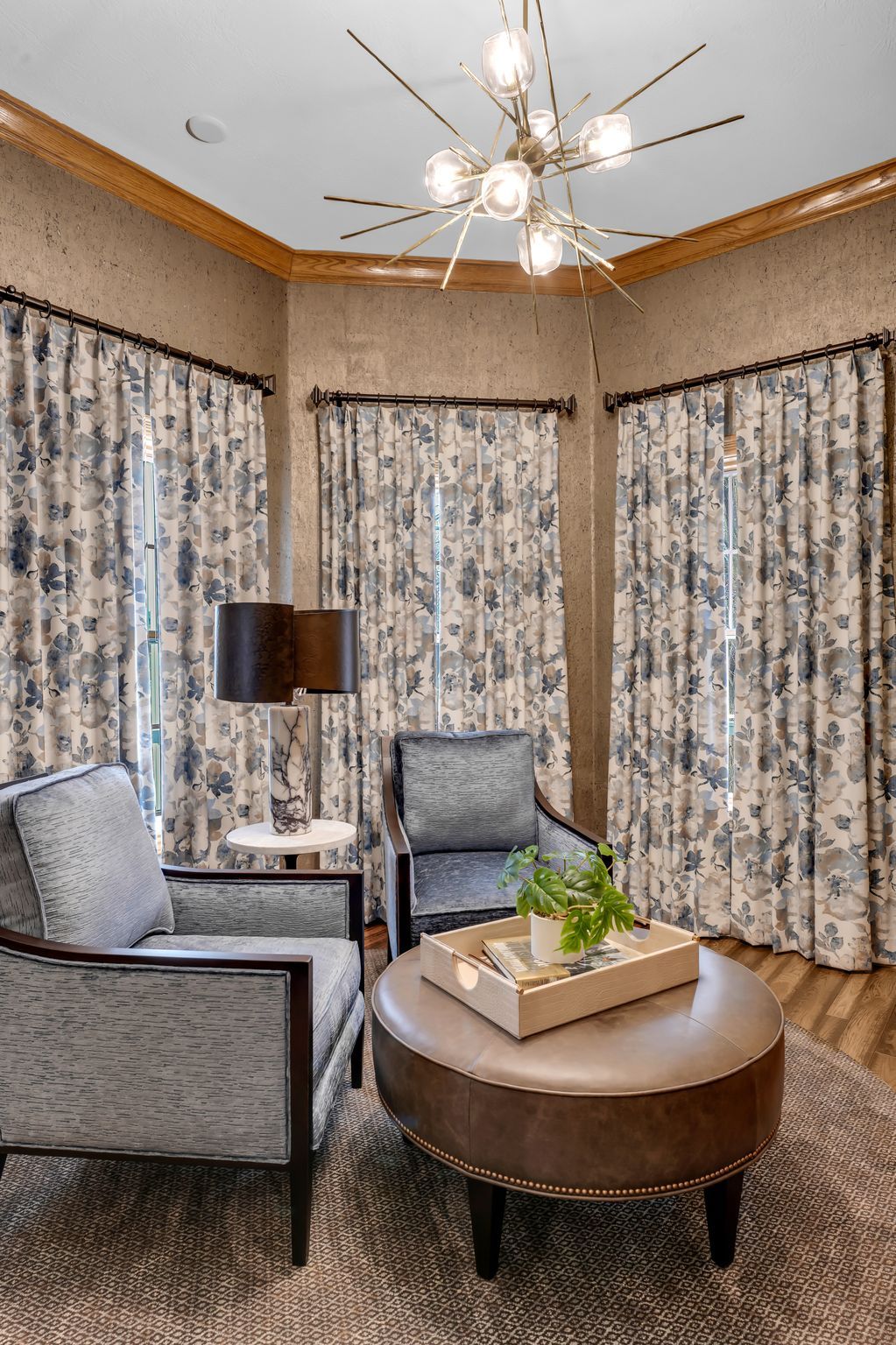 Living room with two armchairs, a round ottoman, and patterned curtains.
