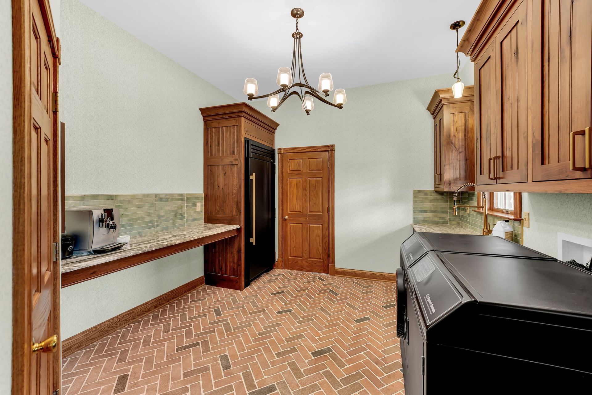 Kitchen with wood cabinets, brick floor, black appliances, and a chandelier.