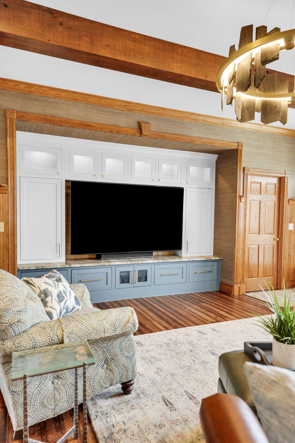 Living room with built-in entertainment center, TV, blue and white cabinets, wood beams, patterned rug, sofa.