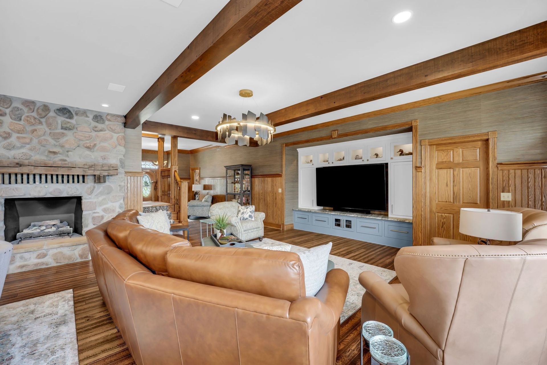 Living room with stone fireplace, brown leather furniture, and TV. Wooden beams and paneling.