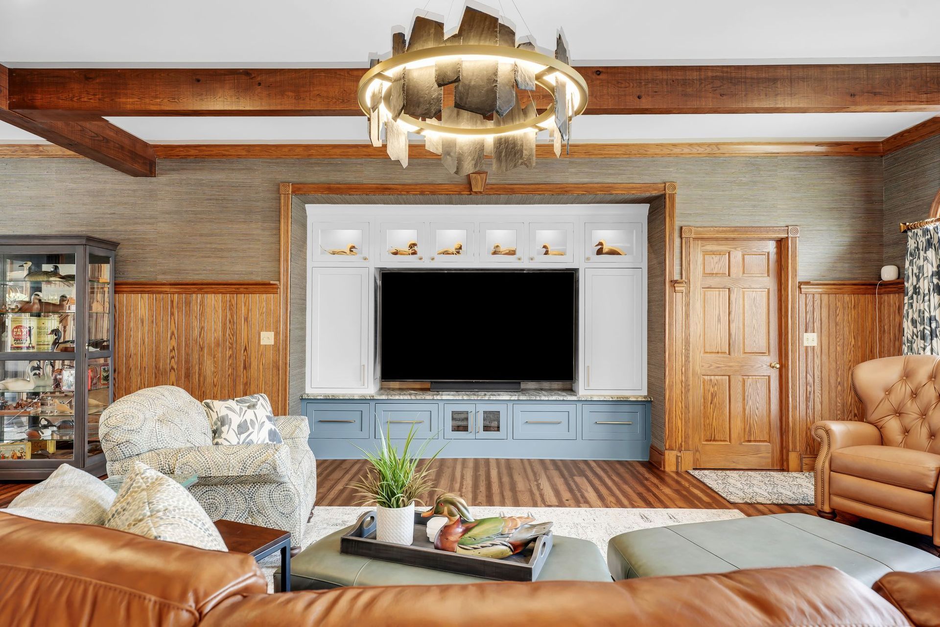 Living room with large TV, wood paneling, blue and white built-in, and leather furniture.