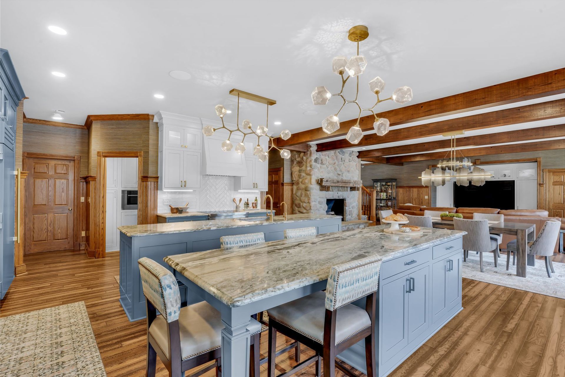 Spacious kitchen with blue islands, granite countertops, wood beams, and multiple light fixtures.