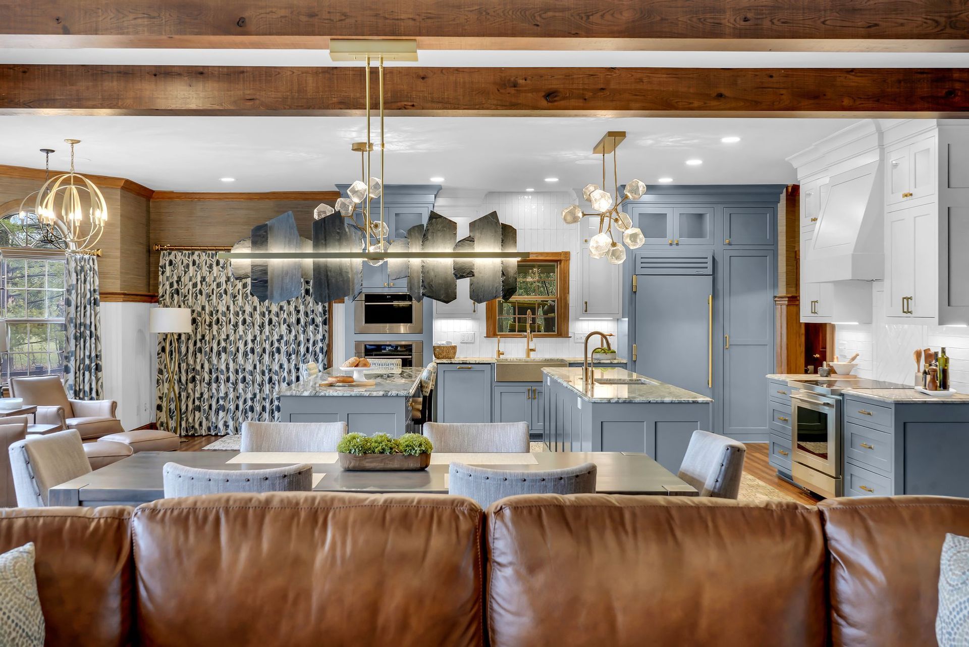 Open-concept kitchen and dining area with blue cabinetry, stone countertops, and a large brown leather sofa.