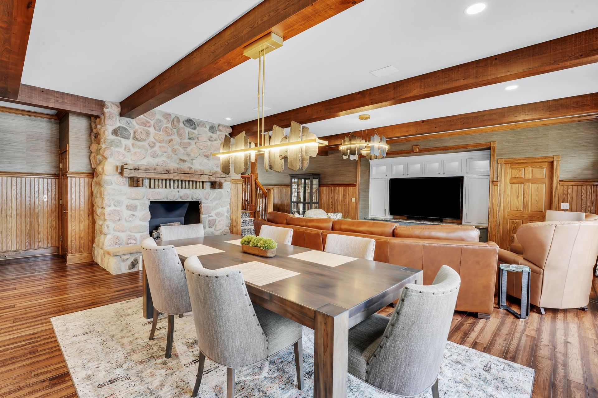 Dining room with stone fireplace, wooden beams, table set for six, and a leather sofa.