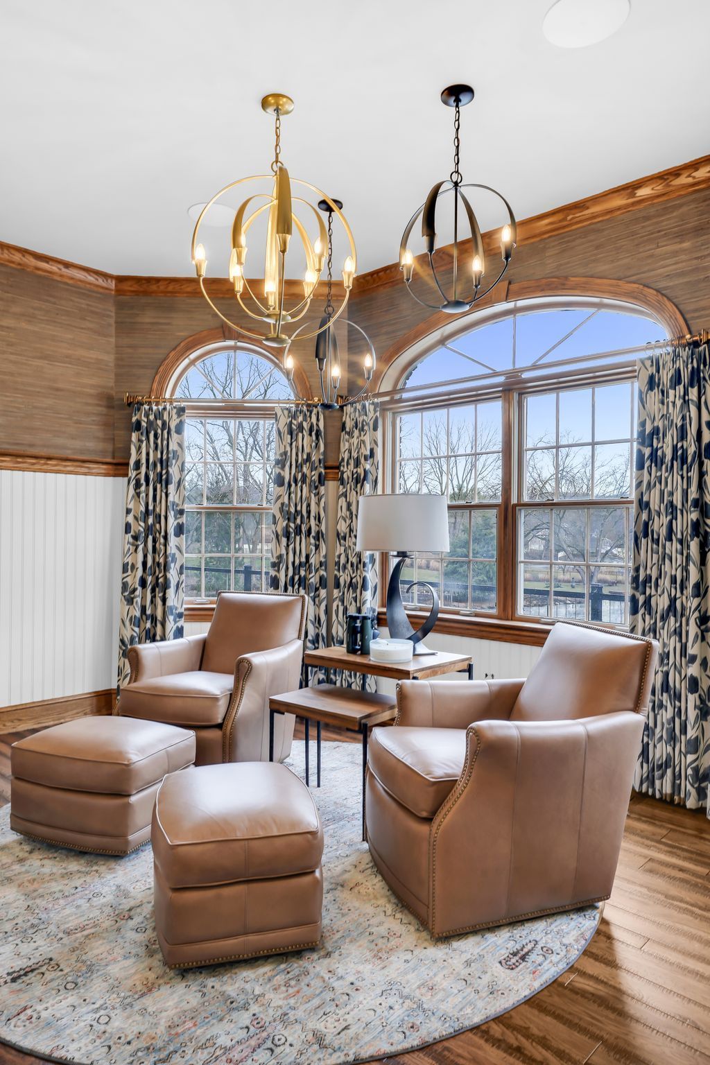 Two leather chairs with ottomans in a room with arched windows, patterned curtains, and two globe pendant lights.