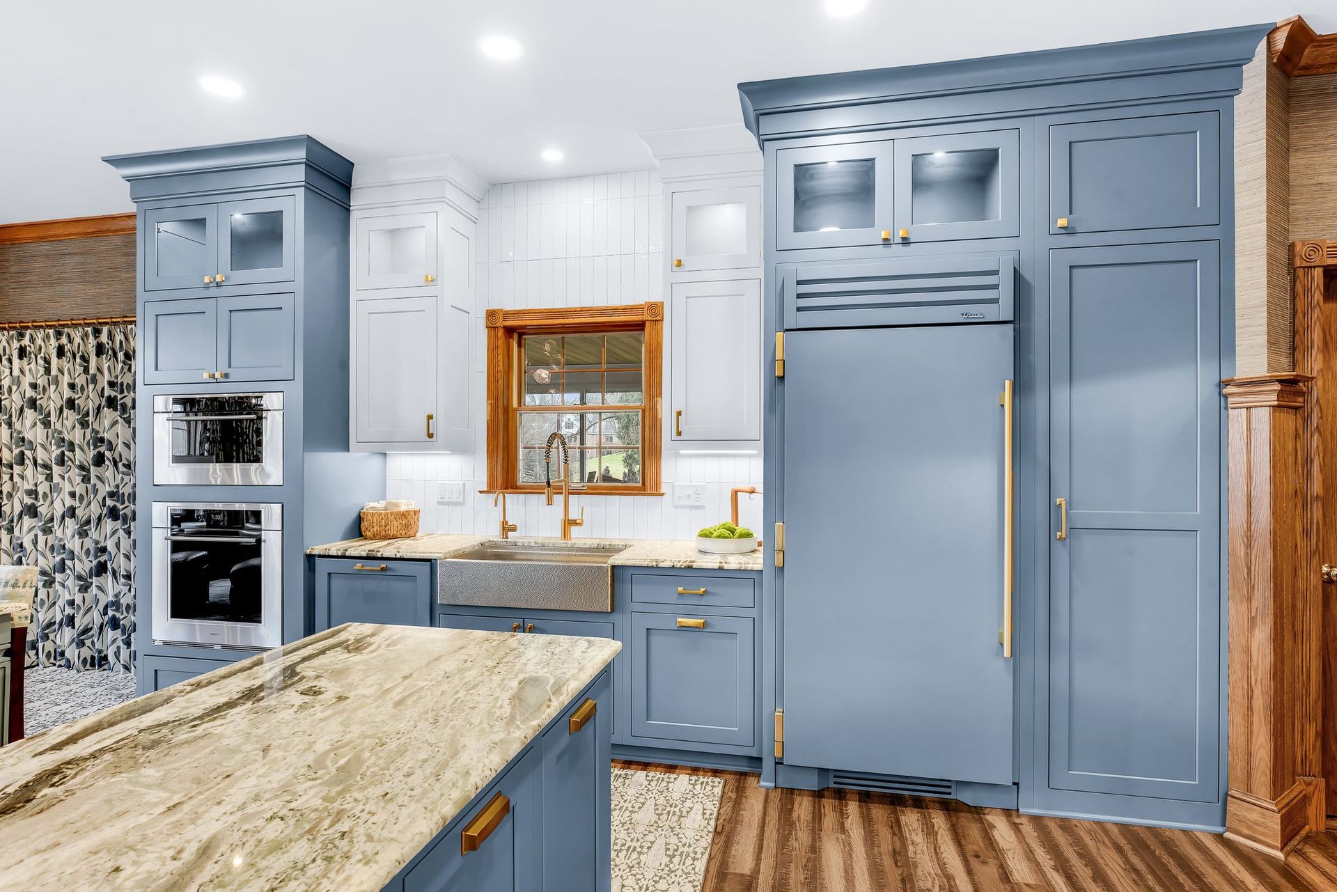 Blue and white kitchen with island, stainless steel sink, gold hardware, and wood trim.