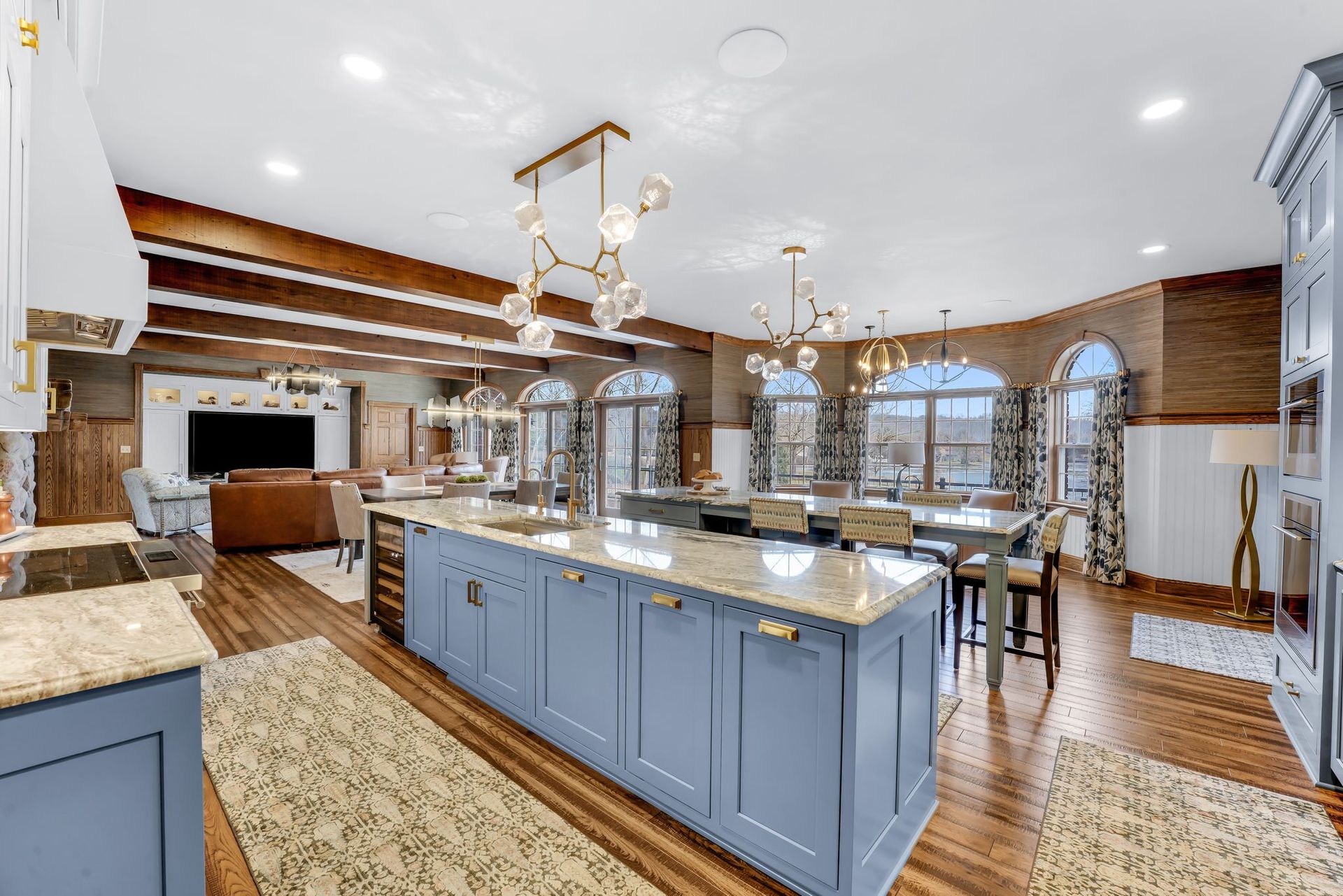 Spacious kitchen with blue island, dining table, and living area with a TV, brick walls, and arched windows.