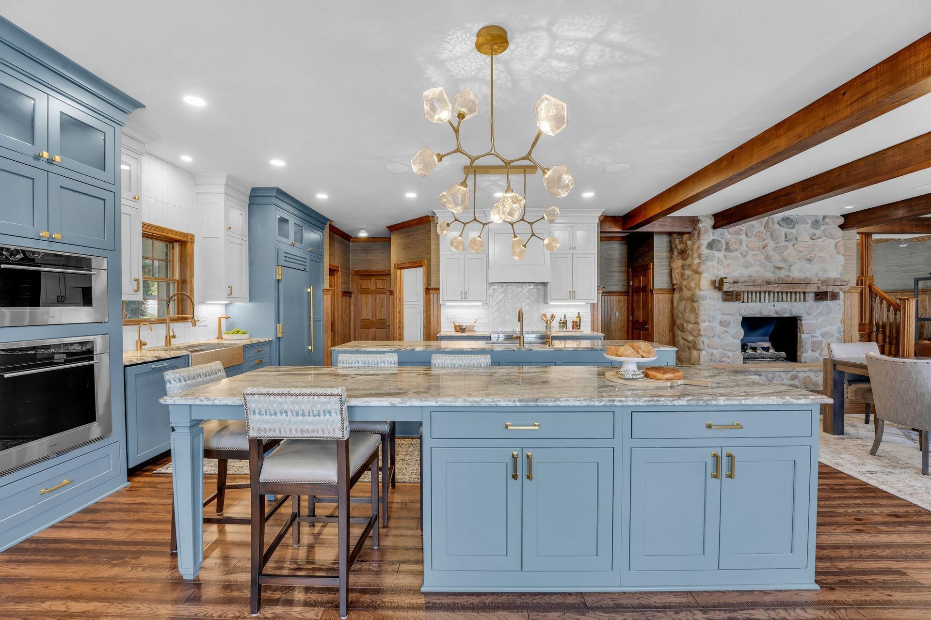 Blue kitchen with island, marble countertops, and gold chandelier.
