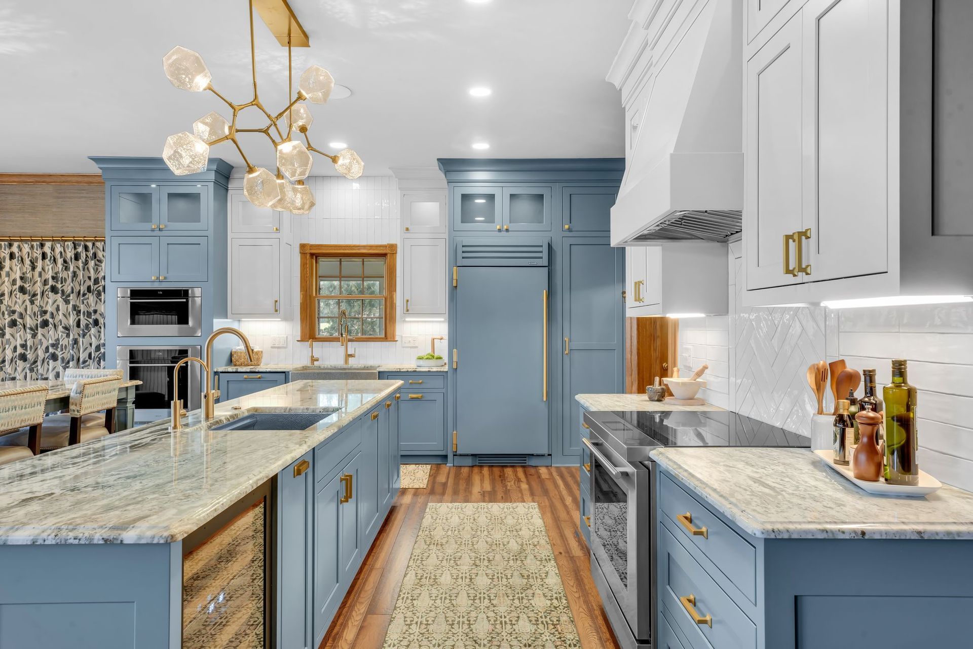 Blue and white kitchen with island, marble countertops, pendant light, and stainless steel appliances.