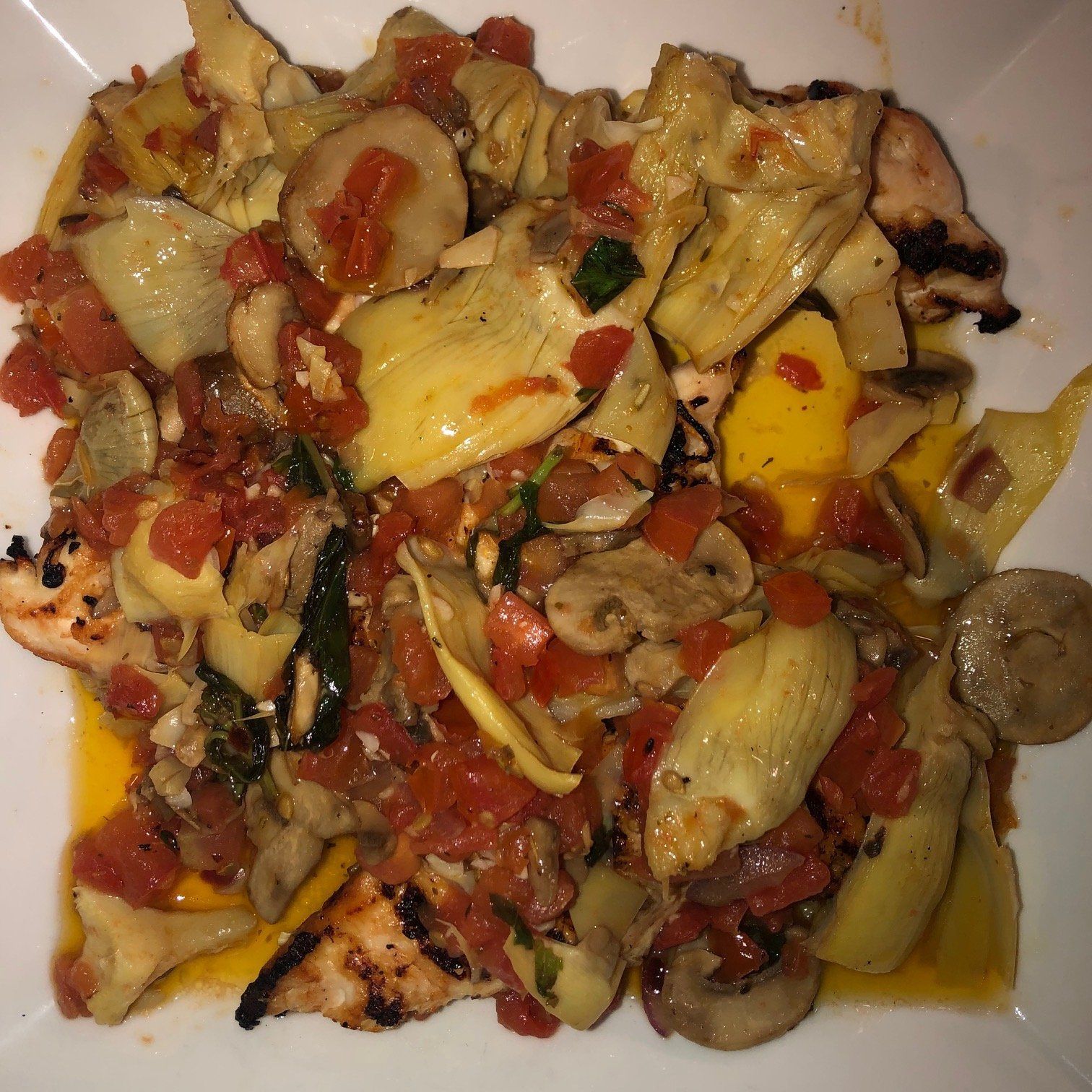 A plate of food with artichokes , mushrooms and tomatoes on a table.