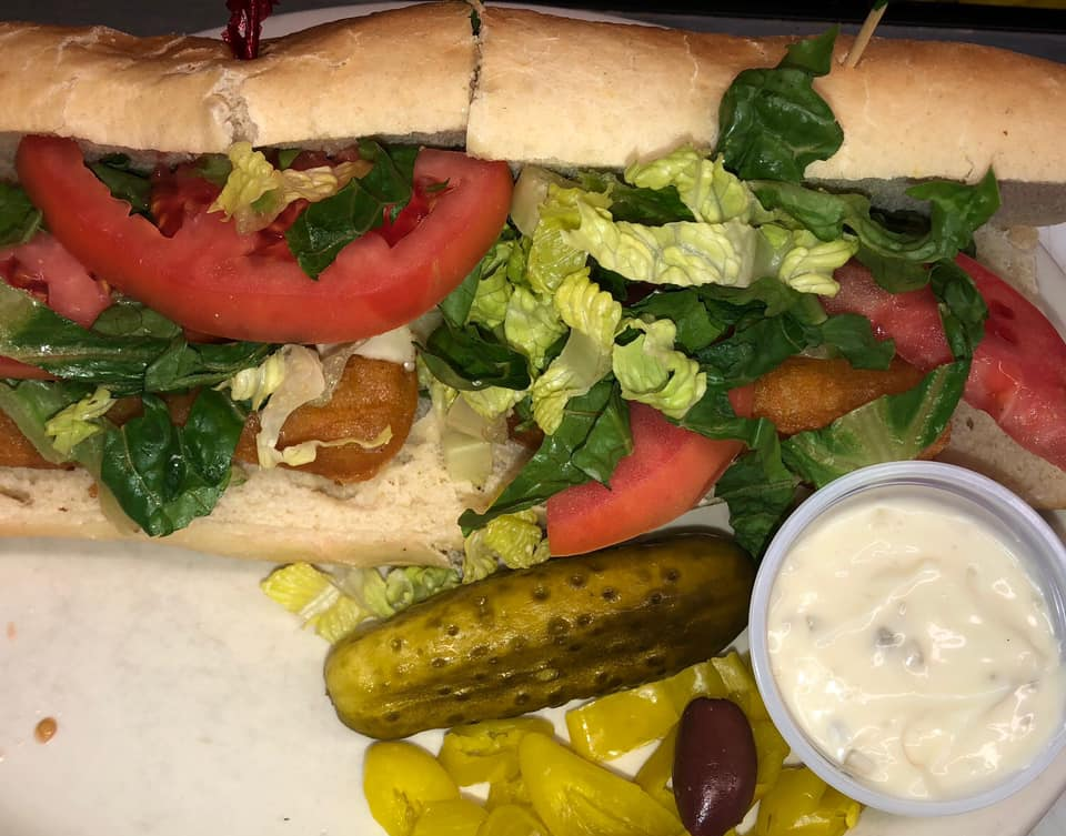 A sandwich with tomatoes, lettuce, olives, pickles, and mayonnaise on a plate.
