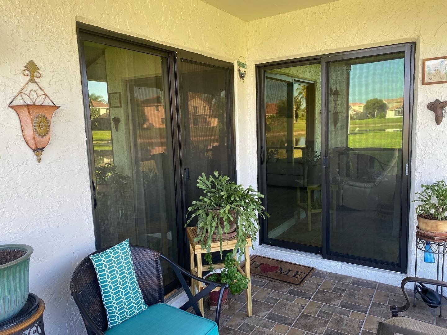 A patio with a chair , table , potted plants and sliding glass doors.