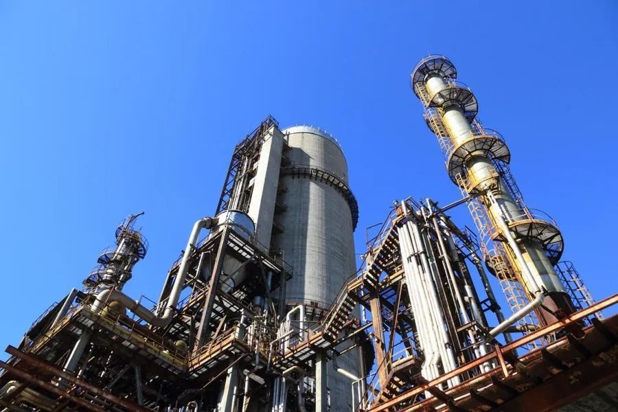 Industrial complex with tall smokestacks against a clear blue sky.