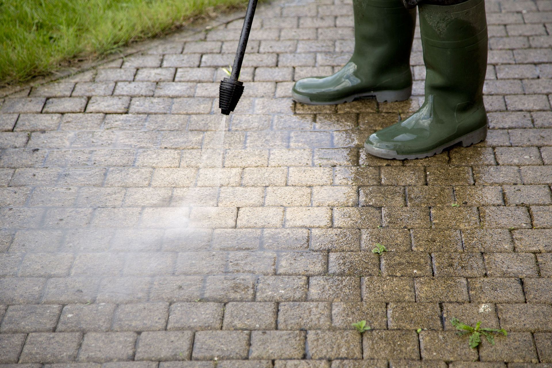 Person in green boots spraying weed killer on a brick path with a hand sprayer.