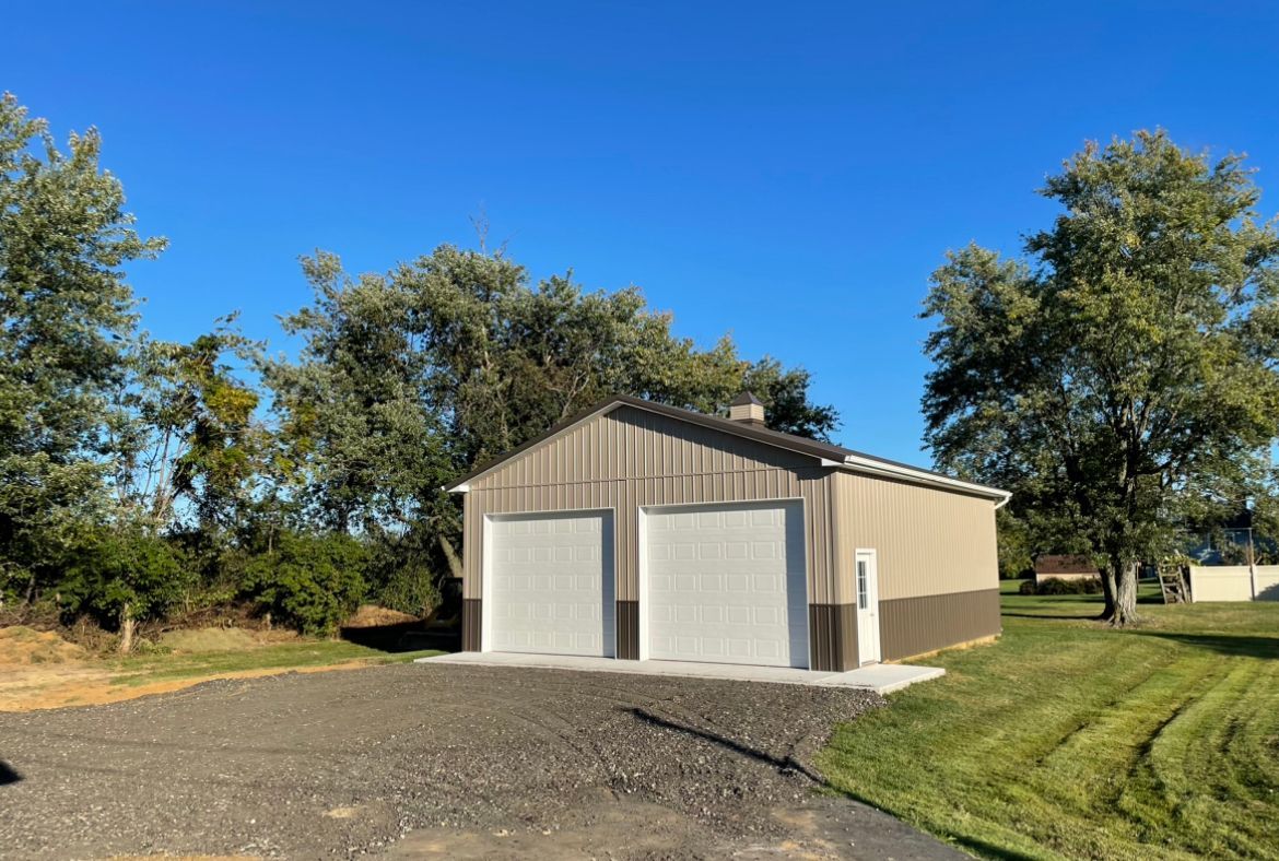 A garage with two garage doors is sitting in the middle of a grassy field.