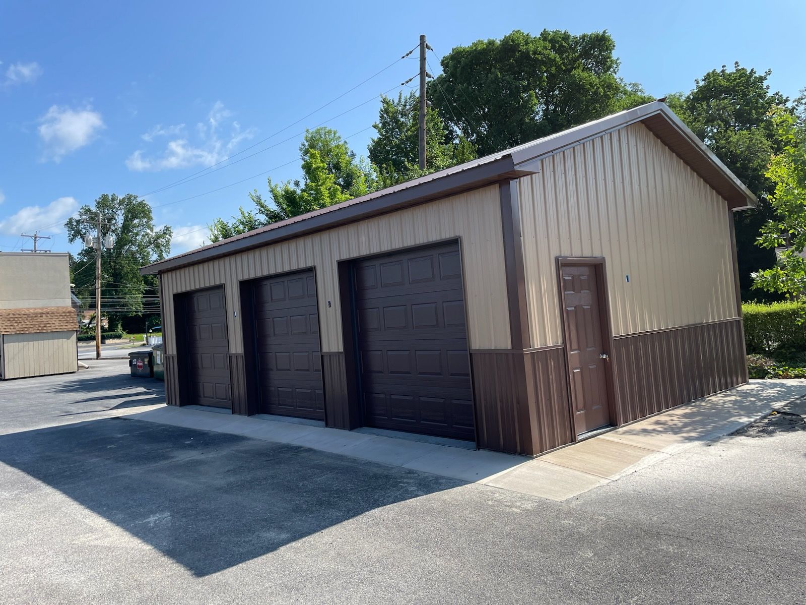 Three-bay garage with brown doors and siding, tan upper walls, on a paved lot.