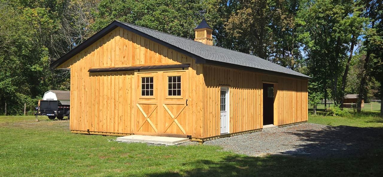 Wooden building with a dark gray roof, two windows, and an open doorway on a green lawn.