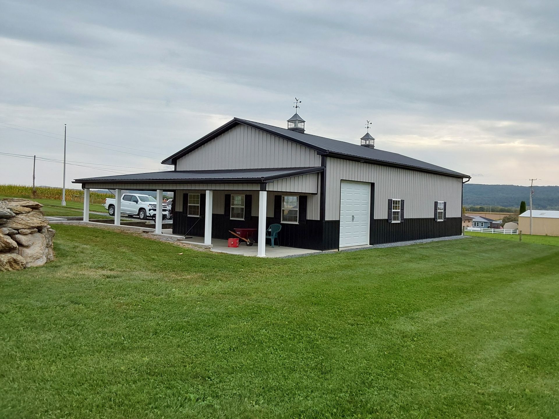A large barn with a porch in the middle of a grassy field.