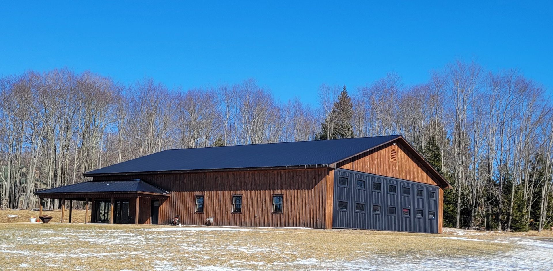 A large wooden barn with a black roof is sitting in the middle of a snowy field.