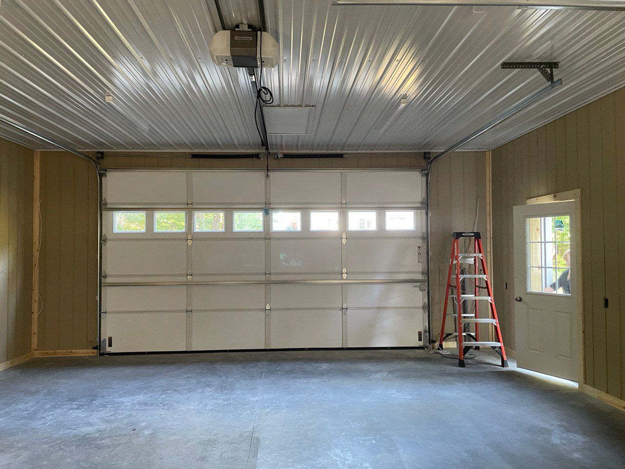 Interior of a garage with a closed white door. A red ladder stands near the door on the right.
