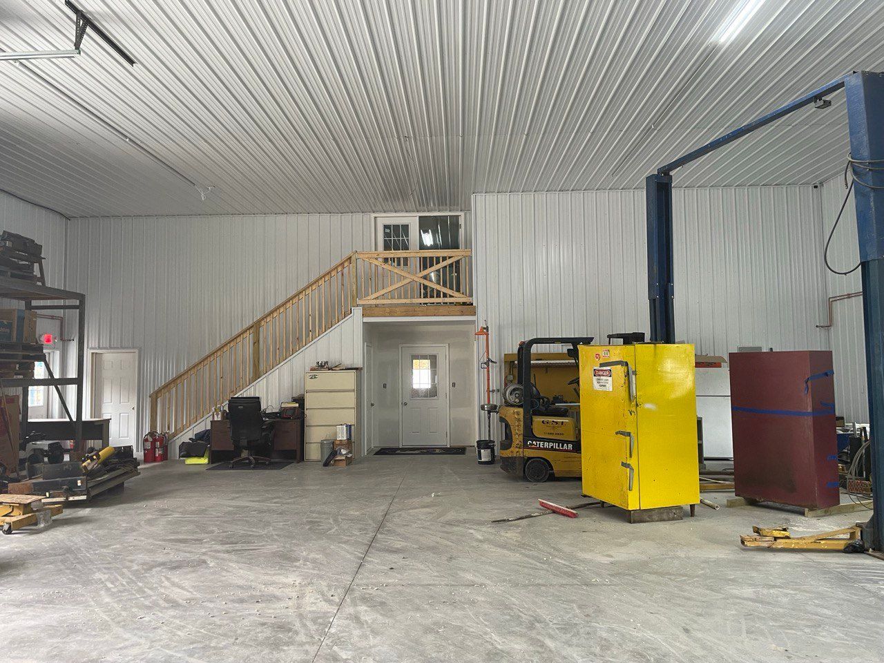 Interior of a large garage with a staircase leading to a small loft area. A forklift and other equipment are present.