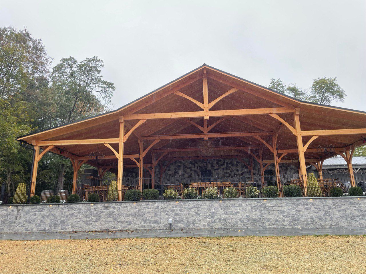 Wooden open-air pavilion with stone wall backdrop, under a cloudy sky.