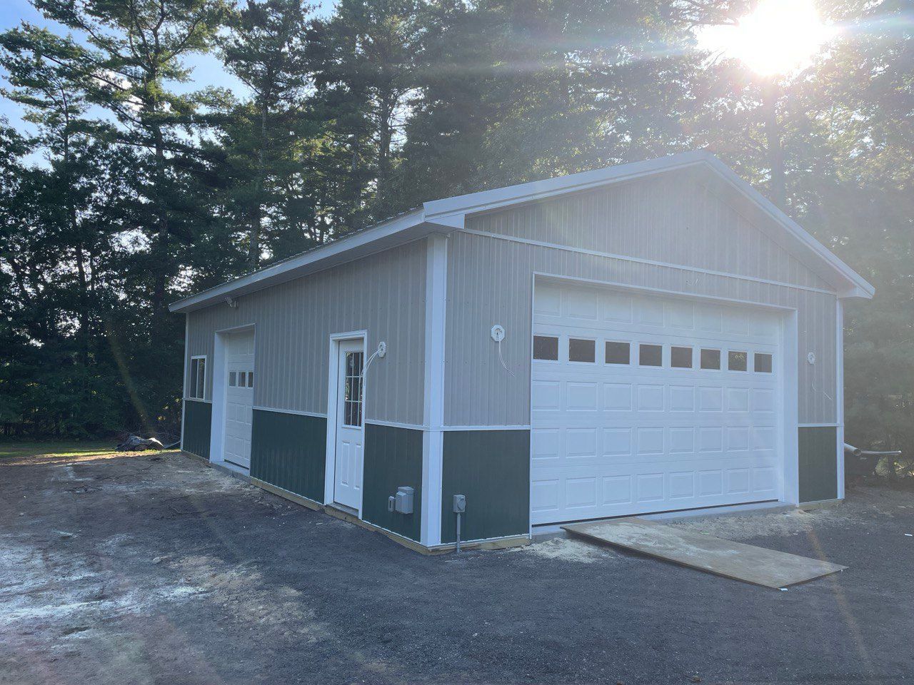 Light gray metal garage with white garage doors and green trim.