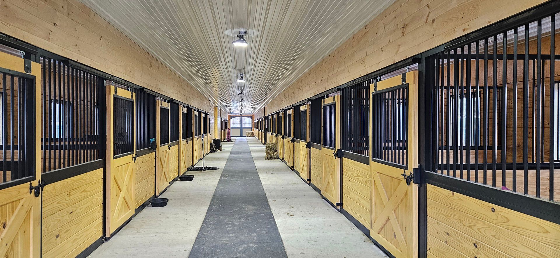 A long hallway filled with rows of wooden horse stalls.