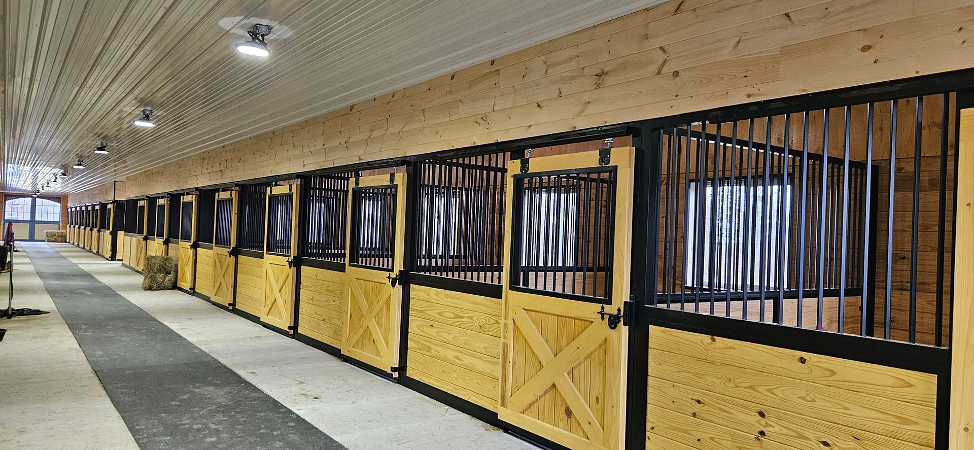 A row of horse stalls in a barn with a black railing.