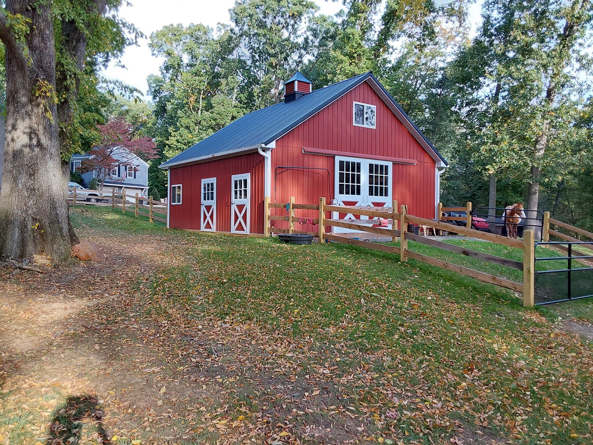 A red barn with a blue roof is surrounded by trees and a wooden fence.