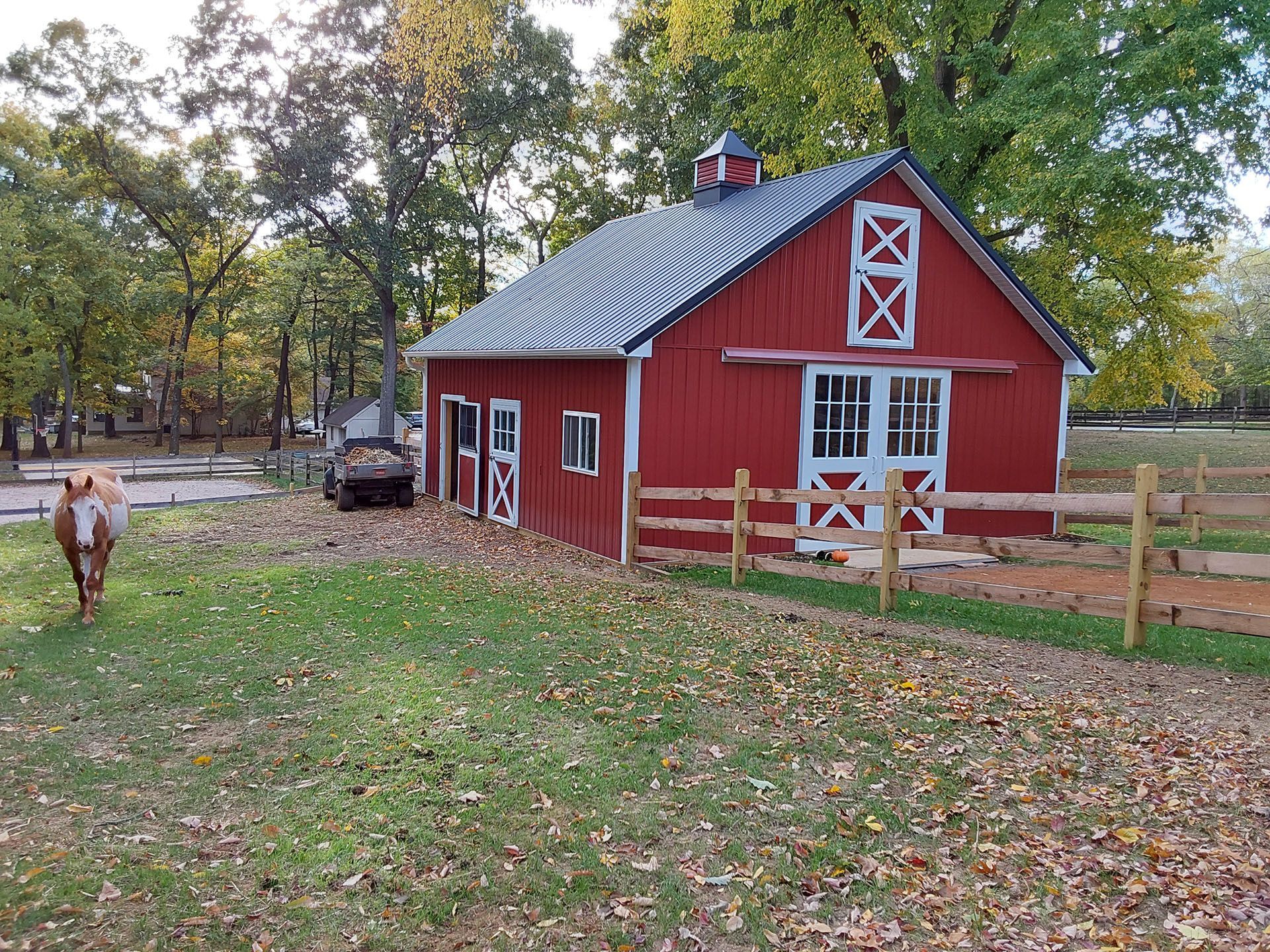 A horse is standing in front of a red barn.