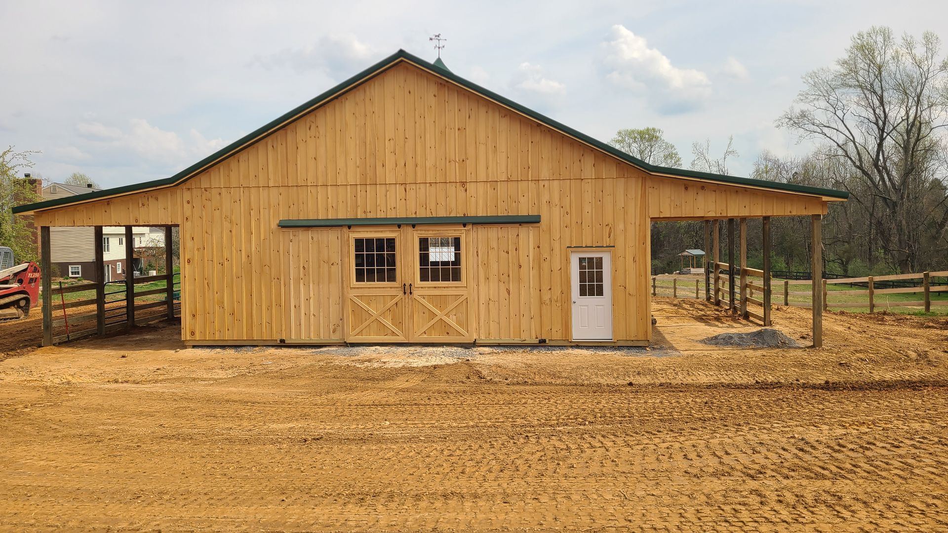A large wooden barn is sitting in the middle of a dirt field.