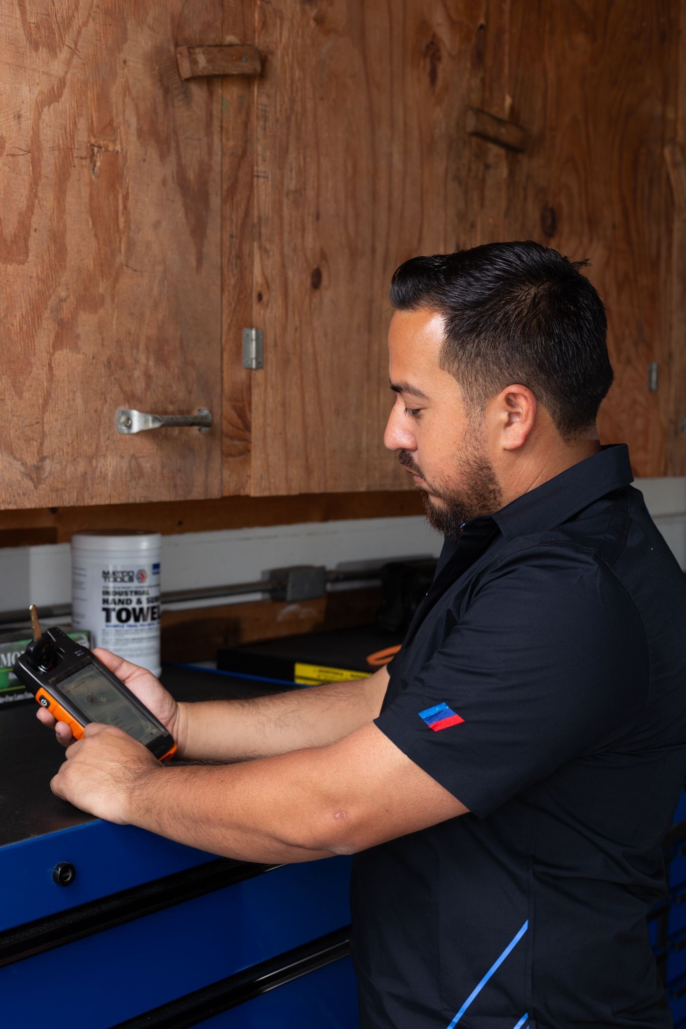 Man in a dark shirt uses a tablet in a garage setting, pointing at the screen.