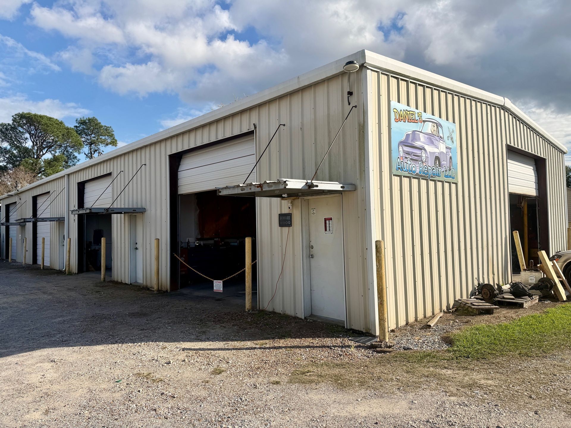 A metal building with several open bay doors, gravel lot, cloudy sky. 