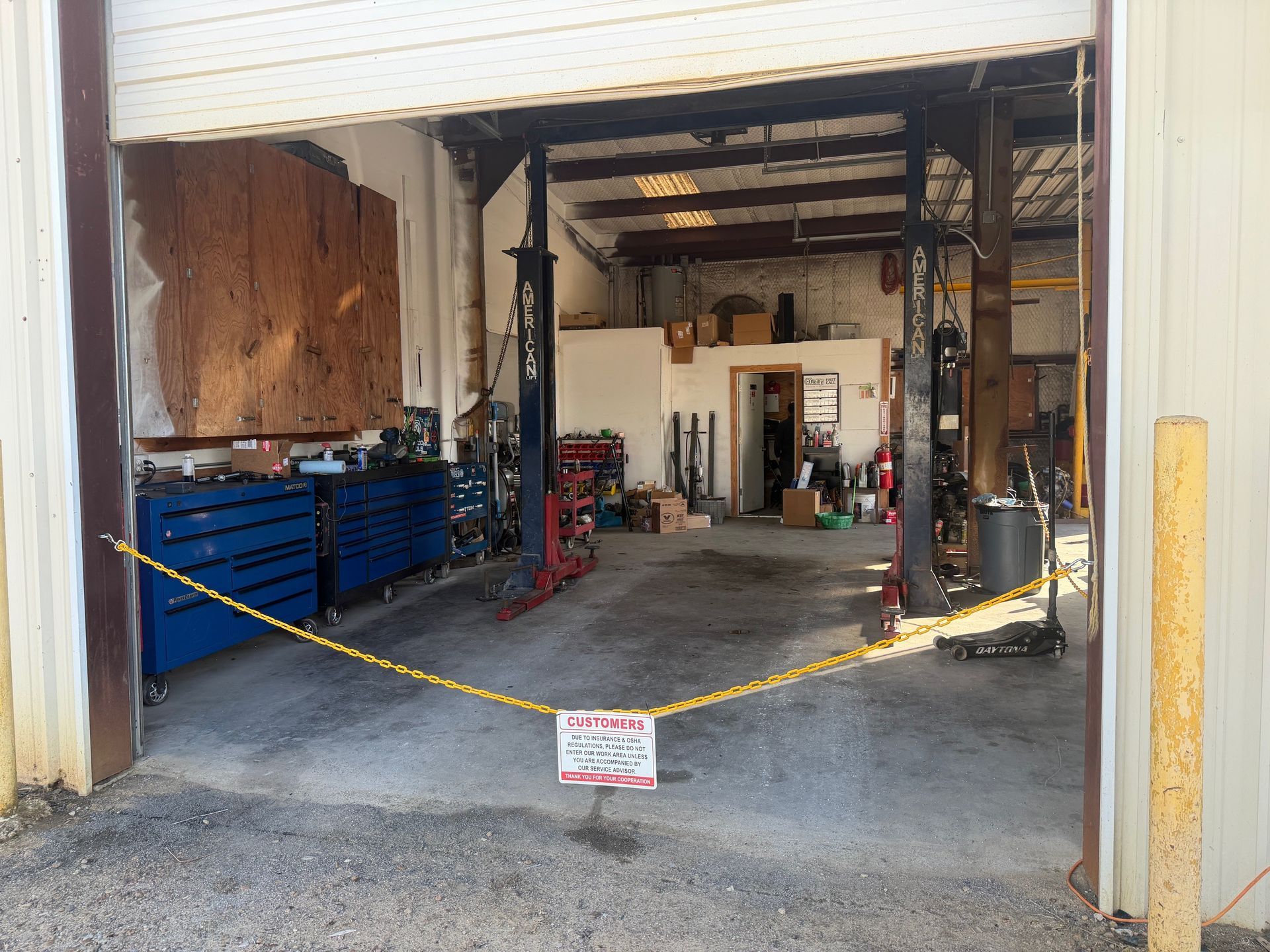 Open garage with yellow caution tape, featuring car lifts, tools, and a sign.