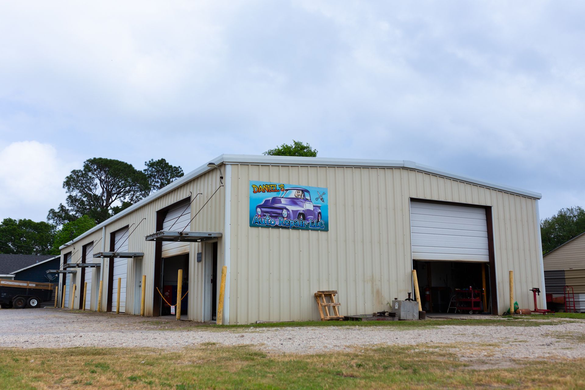 Large, light-colored metal building with several garage doors and a purple truck mural on the side. Overcast sky.