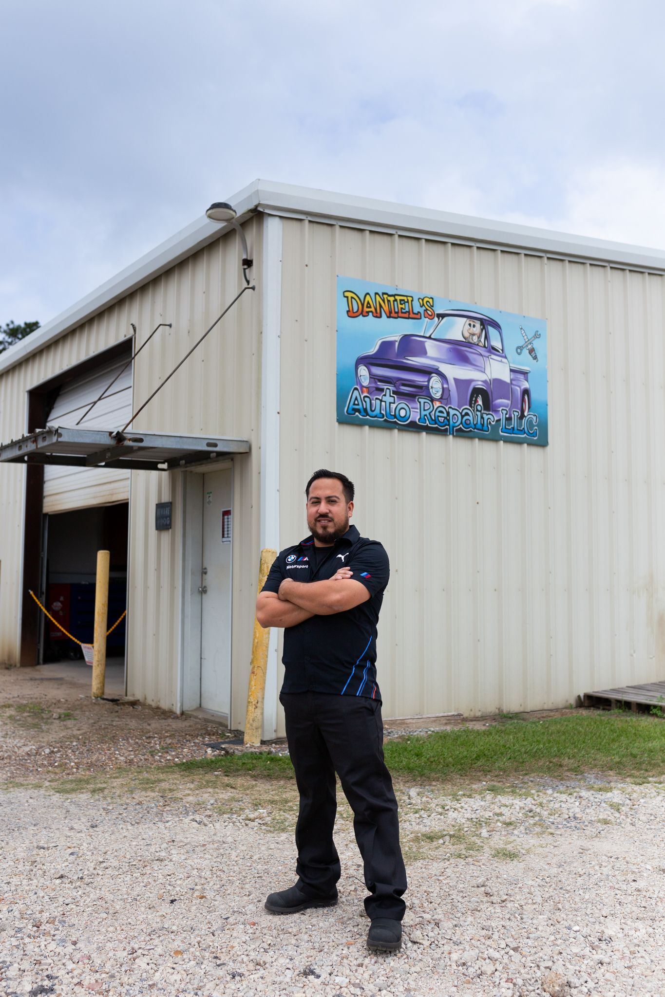 Man in black uniform stands outside a garage with a mural of a purple vehicle.