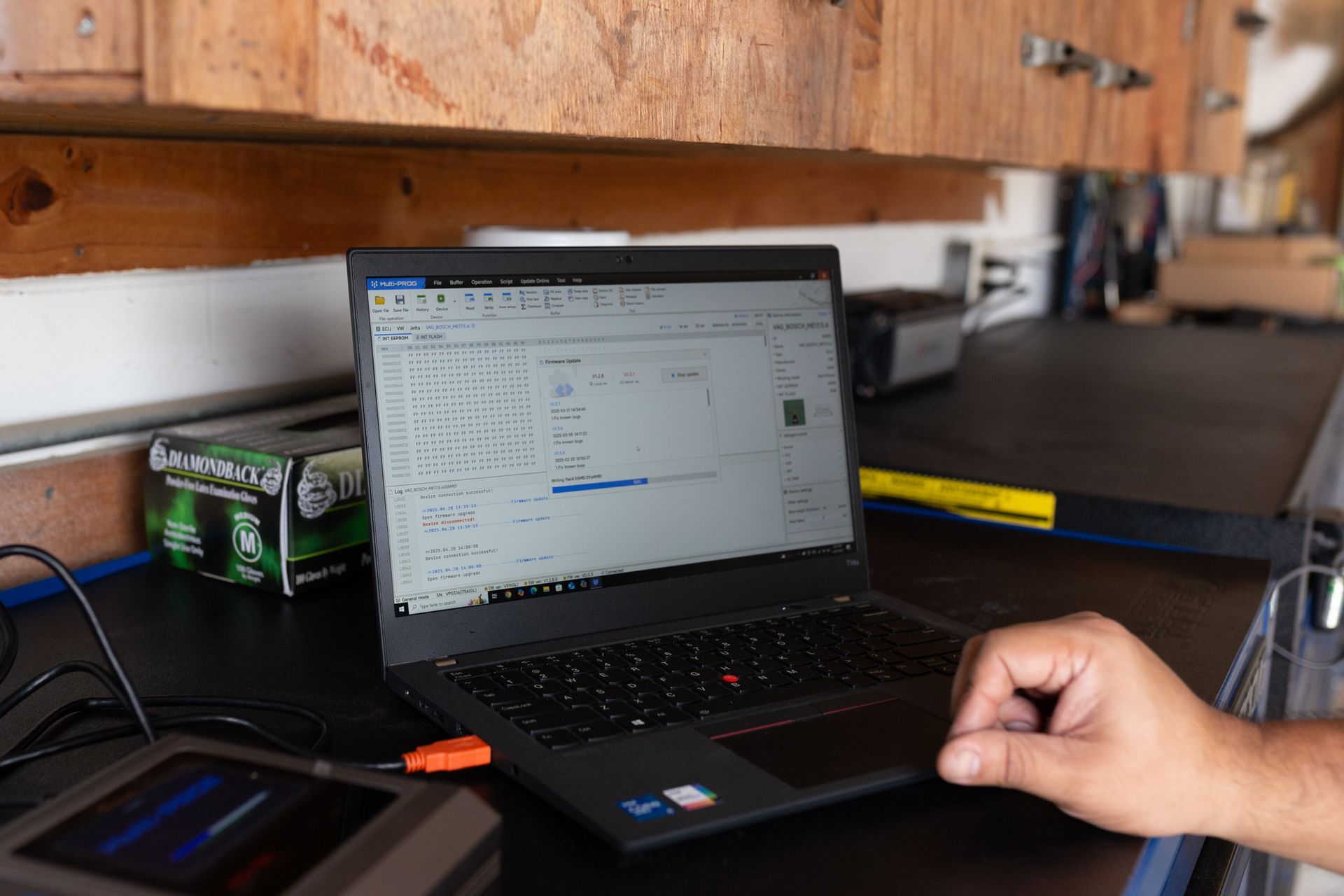 Laptop open on a workbench with a hand nearby, likely in a garage setting, displaying data or charts.