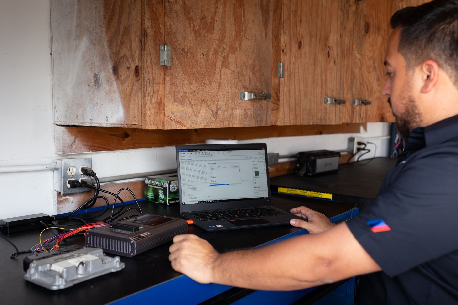 Mechanic using laptop to diagnose vehicle computer in a workshop.